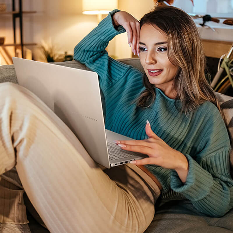A young woman sits on the sofa while she uses an ASUS Vivobook S16 laptop