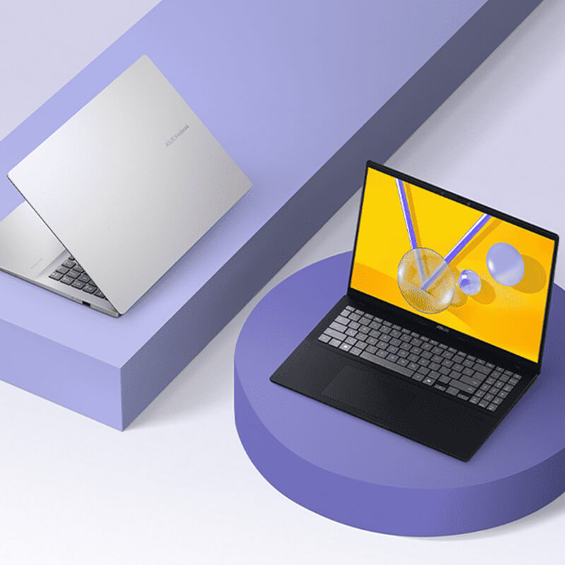 Two ASUS Vivobooks sit on purple geometric shapes. The Silver model is slightly open and oriented to the left while the Black model is open and facing forward.