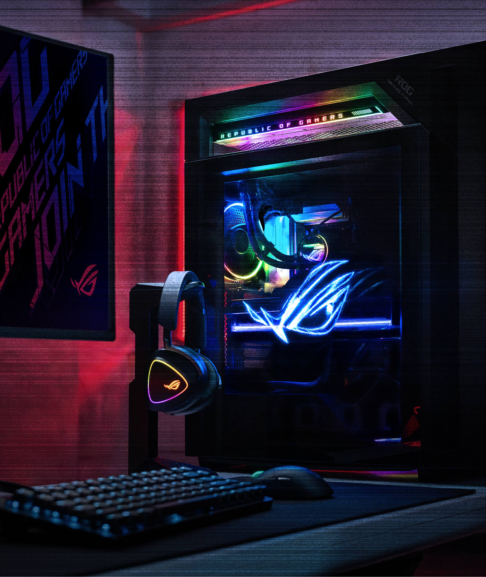 An ROG G1000 desktop with RGB lighting sits beside a gaming keyboard and headset in a dark room, with the Microsoft Windows logo displayed in the lower-right corner.