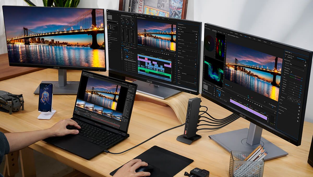 A laptop is put on the table with three monitors connected in front of it. Some of the screens show a stunning night view of the bridge, while others display video editing of the same bridge. There’s a Zenfone next to the laptop.