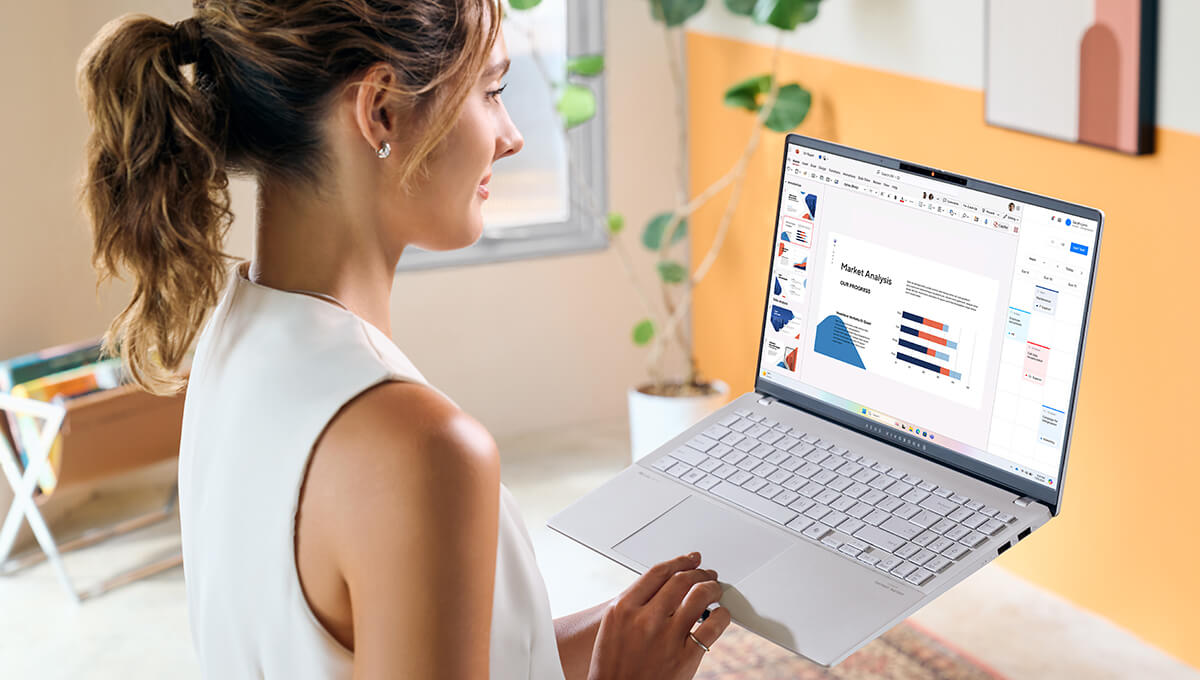a young woman using ASUS Vivobook S 15 laptop while holding it in one hand with Microsoft Copilot AI tool launched and helping with making a slideshow