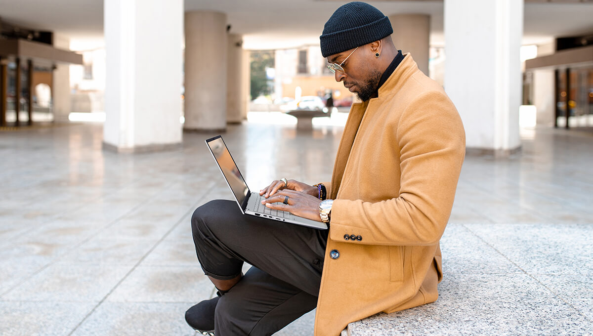 a man holding the ASUS Vivobook S 15 laptop on his laptops while sitting outdoors