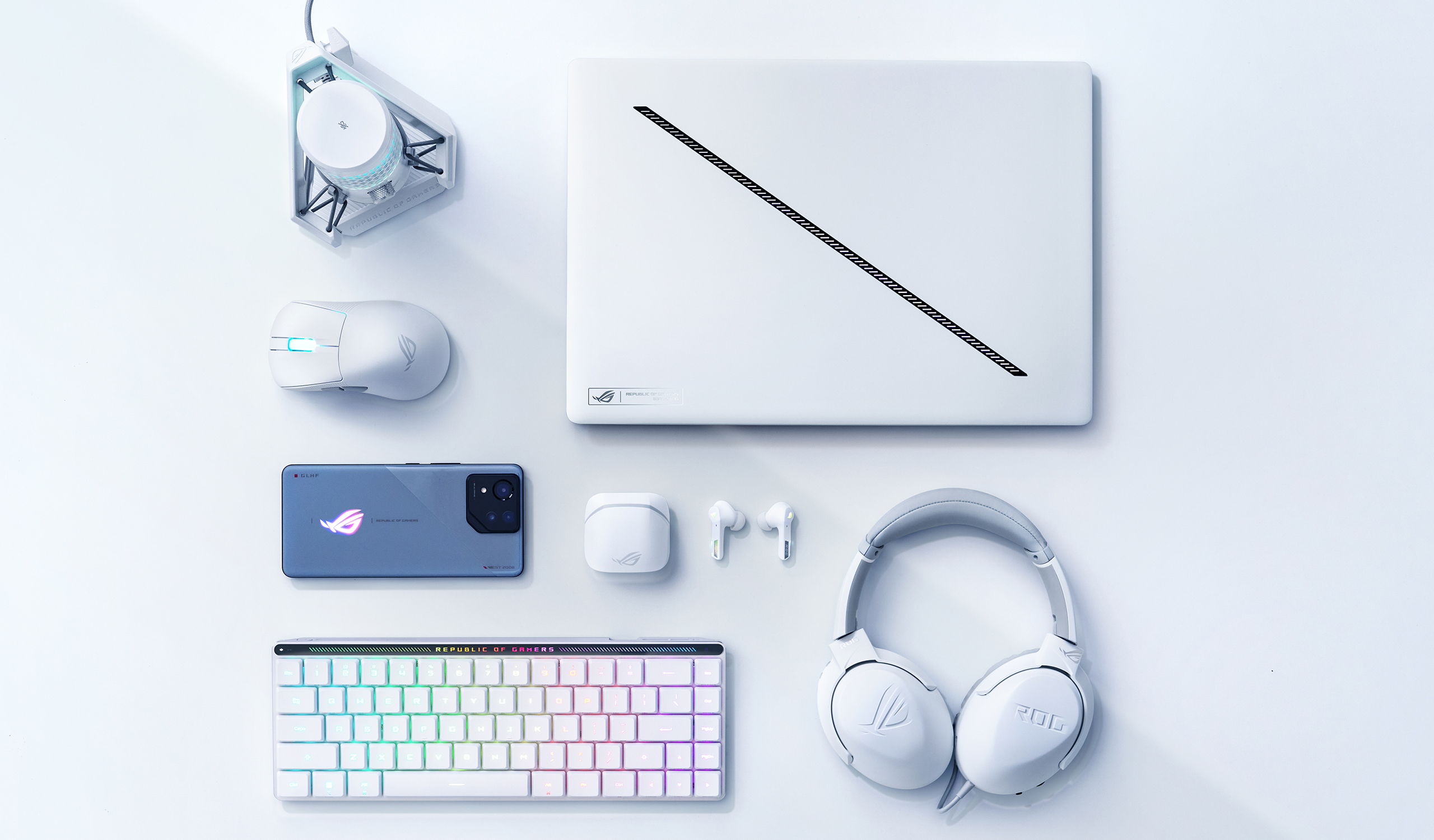 A Platinum White Zephyrus G16, arranged near an ROG mouse, carrying case, and its power adapter.