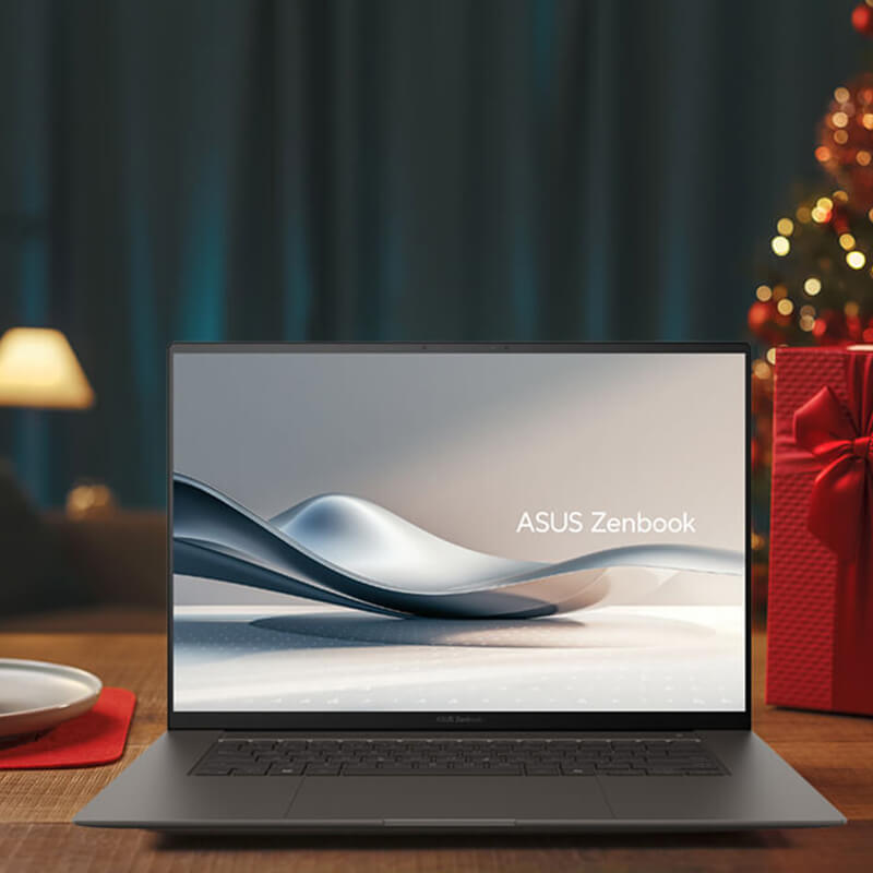 An ASUS Zenbook is placed on a wooden table with holiday decorations around it and in the background.