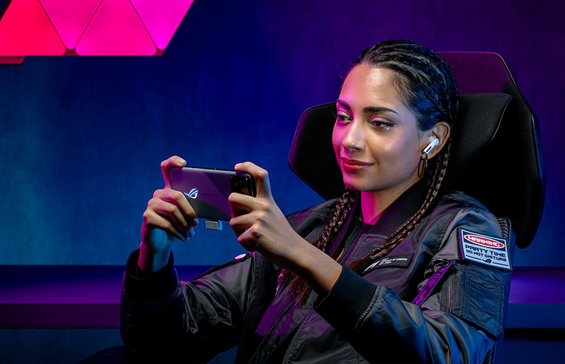 Gamer wearing headphones playing a mobile game in a colorful gaming setup.