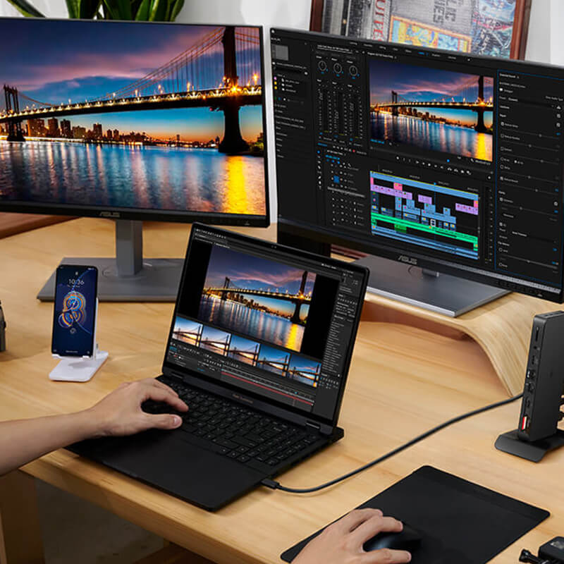 A laptop is put on the table with three monitors connected in front of it. Some of the screens show a stunning night view of the bridge, while others display video editing of the same bridge. There’s a Zenfone next to the laptop.