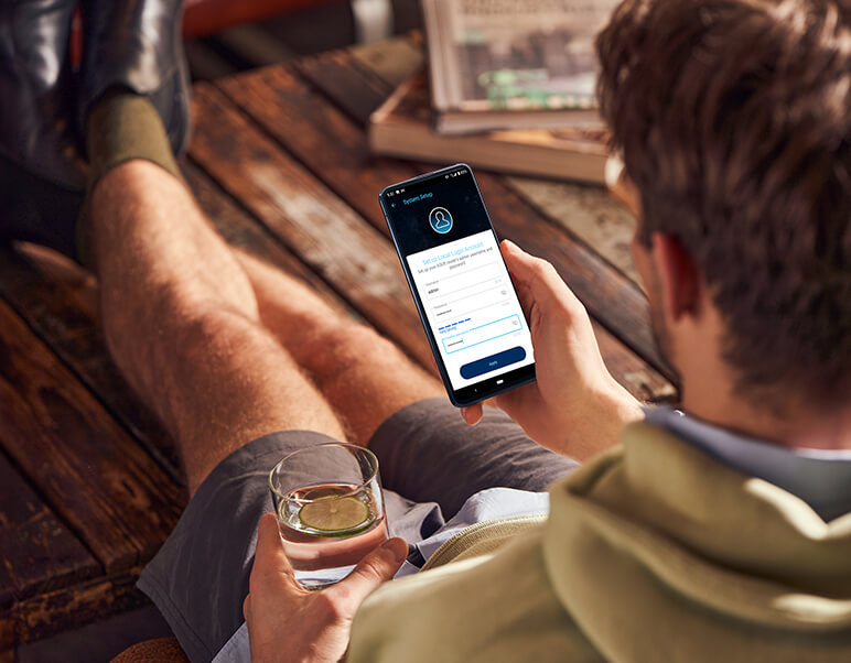 Een man zit op de grond en gebruikt zijn smartphone, waarop de installatie-interface van de ASUS Router-app wordt weergegeven.