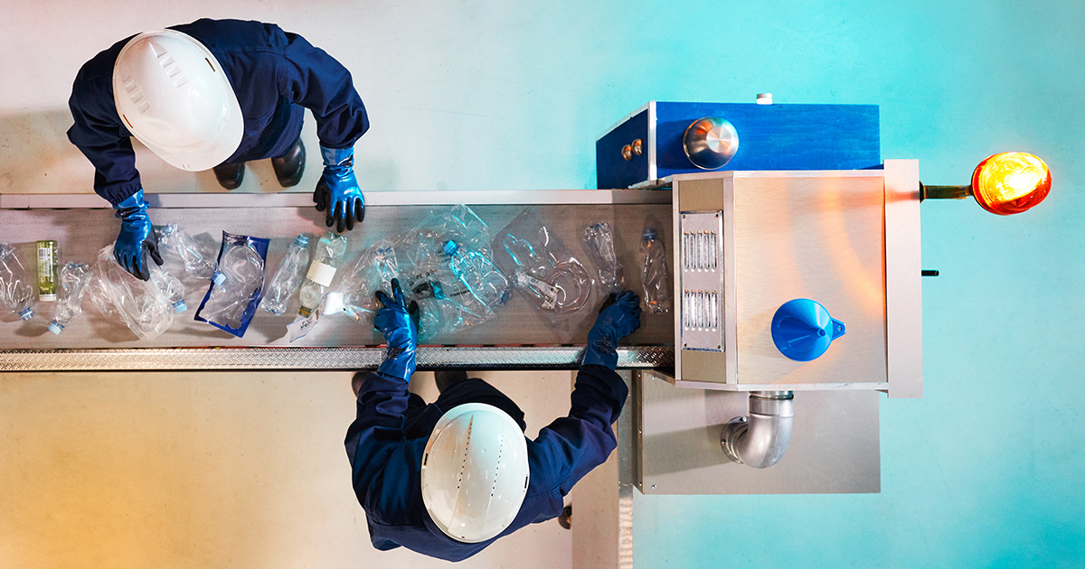two workers sorting post-consumer recycled plastic on a conveyor belt