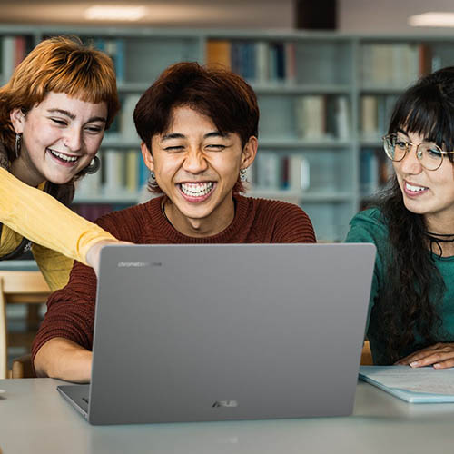 Four students gather around an open ASUS Chromebook laptop that sits on a table in a library